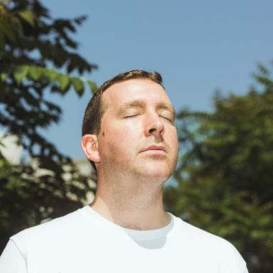 Joe wears white t-shirt and looks to sky with eyes closed