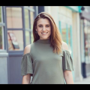 miri wears a grey top and smiles at the camera. her medium length hair is swept to the side.