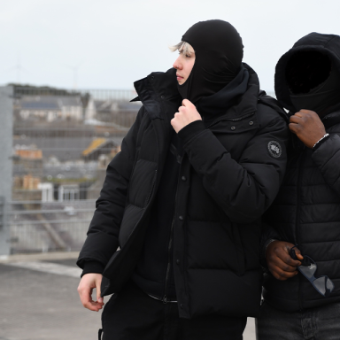 a blonde boy wears a big black puffer jacket and black beanie