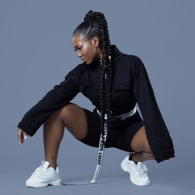 a woman crouches, her braid is long and she wears all black and white trainers