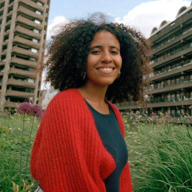 a woman smiles outside some high rise buildings. she is wearing a red cardigan