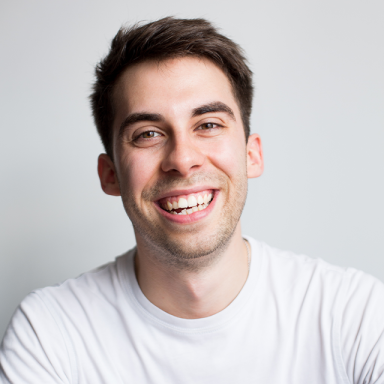 a man with short brown hair smiles and wears a white t-shirt