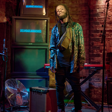 a man with dreadlocks holds a guitar and poses on stage