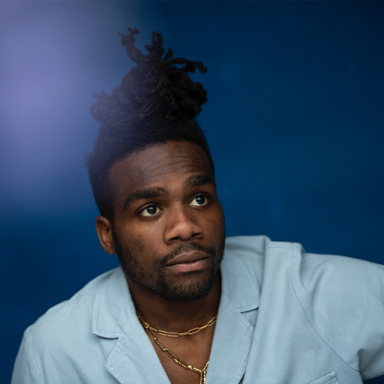 a man wears a light blue shirt has his hair tied back in an updo