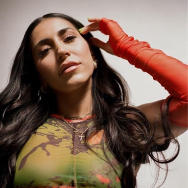 a woman with dark hair poses in a multi coloured long sleeve top