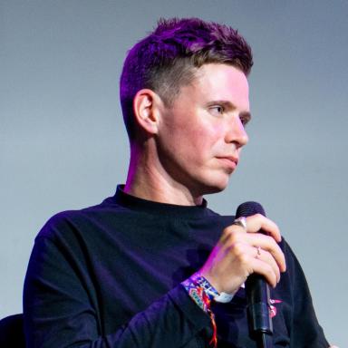 a man wearing a black long sleeve top holds a microphone 