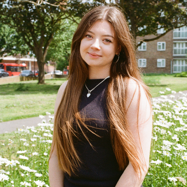 a woman with long brown hair and a black sleeveless top smiles in a field of daisies