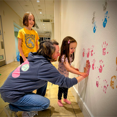 child putting paint handprints on the wall with guidance from an adult