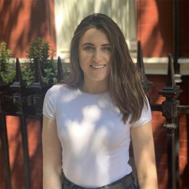 a woman with brown hair wears a white t shirt and stands in the shade