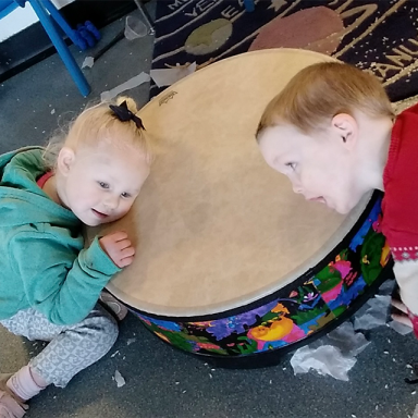 two children put their ears to a drum