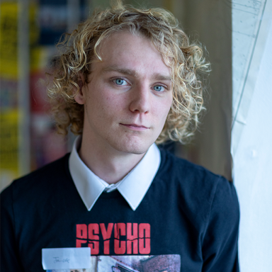 a person with blonde curly hair and a sweatshirt with white collar