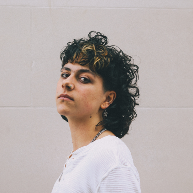 a person with dark curly hair wears a white top