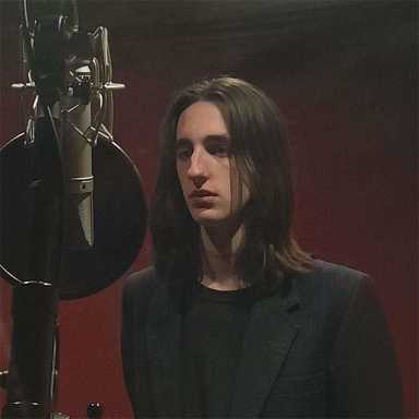 a man with long brown hair is in a recording booth behind a mic