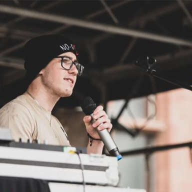 a man holds a microphone and wears glasses and a black beanie